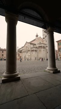 Modena, italy, april 12, 2026. Personal point of view while walking under the porticoes of piazza grande in modena, italy. The romanesque cathedral and ghirlandina tower are visible