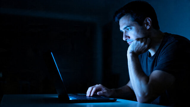 [Man] [with tired mood] [working at a laptop in the dark]