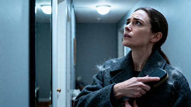[Young woman] [with anxious mood] [trying to remove pet hair from her coat with a lint brush in a hallway]