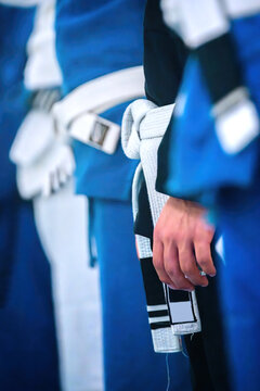 View of martial artists standing in a row wearing blue uniforms and white belts with a focus on a tied knot and a hand.