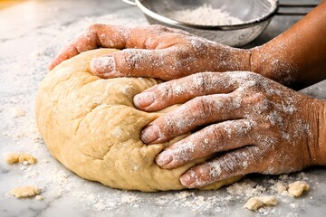 Fototapeta premium Hands kneading fresh dough dusted with flour on a marble surface with a sieve in the background