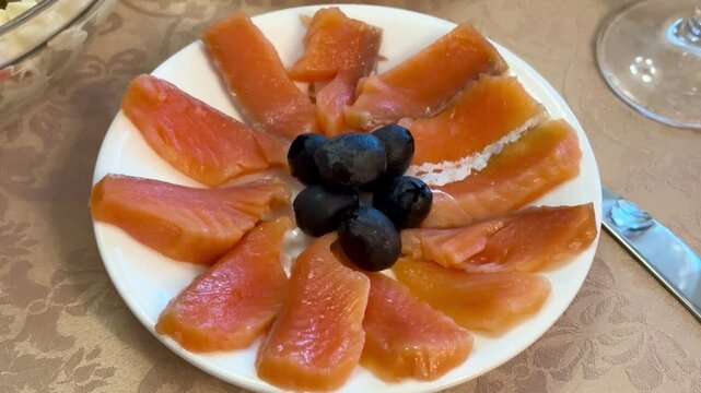 Red trout slices with olives plated on white porcelain plate arranged in floral pattern with light salt sprinkle beside vintage