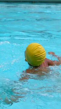 Boy pushing off pool wall swimming laps during swim training turning head breathing yellow swim cap