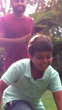 Vertical video: Running child in polo falling, grabbing football in yard as adult playfully chasing