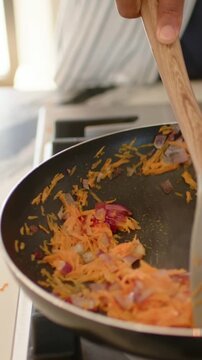 Vertical video: Spatula entering cook scraping carrot and onion in pan at stove to cook striped top