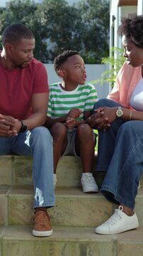 Vertical video: Starting child telling story and gesturing on front stone steps, parents leaning in