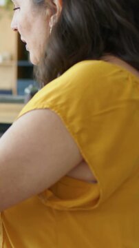 Vertical video: Hearing friend, mature woman in mustard leaning, reaching across table at home, cup