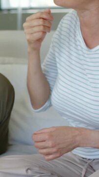 Vertical video: Shifting, woman in striped top raising hand to mouth on sofa at home during chat