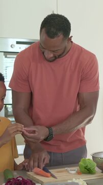 Vertical video: Entering dad salmon tee guiding son, teaching peeling and slicing carrot at island