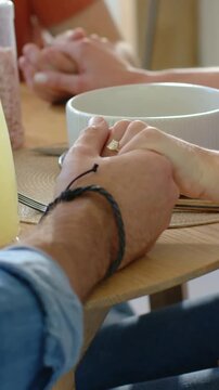 Vertical video: Holding hands, denim-pink couple shifting watch into view and showing ring at table