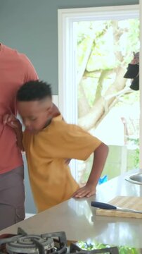 Vertical video: Coming dad urging kid in yellow tee putting on black backpack at island to school