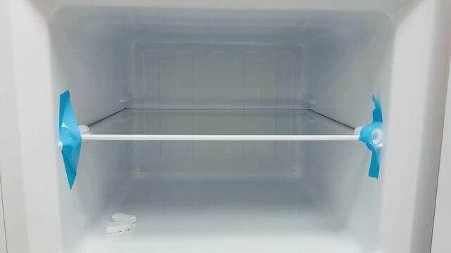 Empty freezer interior new refrigerator showing wire shelf with protective blue tape, open door, pristine white plastic walls