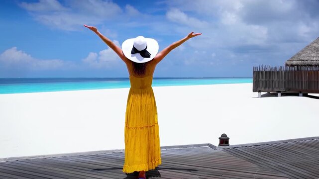 A tourist woman in a yellow summer dress enjoys the beautiful view of a beach in the Maldives islands
