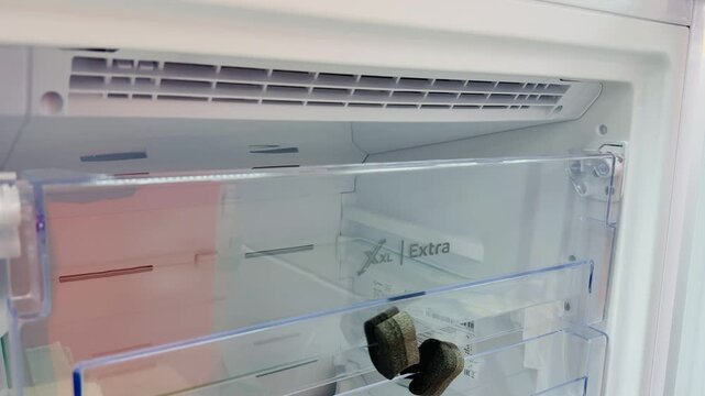 Empty glass shelves inside new refrigerator showcasing pristine interior, clear drawers, chilled vent, soft LED lighting, bright