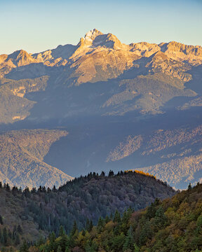 View of the majestic Mount Triglav peak illuminated by golden sunset light over the Julian Alps and dense green forests in Sorica, Skofja Loka, Slovenia.