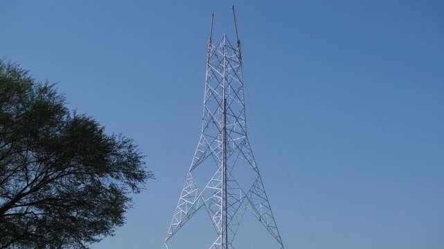 Construction of a new high-voltage electrical transmission tower against a clear blue sky