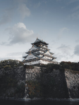 View of the historic Osaka Castle with its white walls and golden ornaments standing above massive stone fortifications under a cloudy sky Japan.