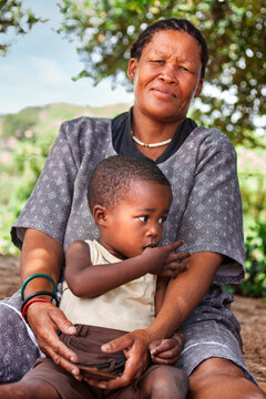 A Basarwa San Mother woman hold in the lap a child, outdoors in the bush in the Kalahari Desert
