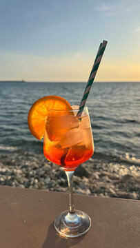 Spritz cocktail with orange slice and striped straw by calm sea at sunset