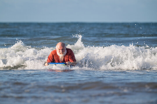 Active senior man boogie boarding toward shore on a sunny summer beach during retirement