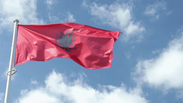 Albanian flag waving in strong wind against blue sky, national symbol of Albania, patriotic outdoor closeup footage