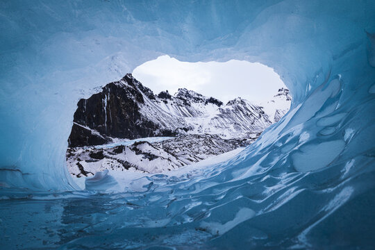 View of the blue ice cave at Falljokull glacier looking out towards snow-covered mountain peaks Sveitarfelagid Hornafjordur, Iceland.