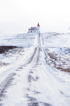 View of the historic Snaefellsnes church with its red roof at the end of a long snowy road winding through a white winter landscape Eyja- og Miklaholtshr, Iceland.