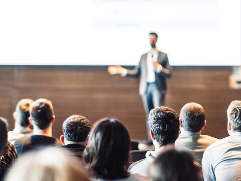 Speaker giving a talk in conference hall at business event. Rear view of unrecognizable people in audience at the conference hall. Business and entrepreneurship concept