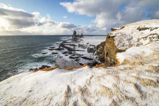 View of the snow-covered Snaefellsnes peninsula coastline featuring the Londrangar basalt cliffs and the rough Atlantic Ocean in Eyja- og Miklaholtshr, Iceland.