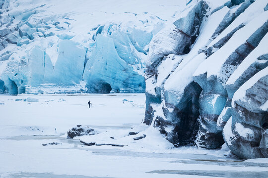View of the Svinafellsjokull glacier with a photographer standing on the ice near massive blue ice formations in Sveitarfelagid Hornaf, Iceland.