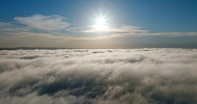 Aerial view flying through clouds. Bright sun disk blue sky background rising above fog summer day. Drone flight high altitude atmosphere scenic nature exploration high angle perspective heaven.