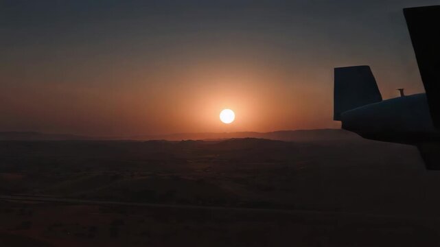 Surveillance drone unmanned aircraft silhouette at sunset dusk with warm glow over desert landscape