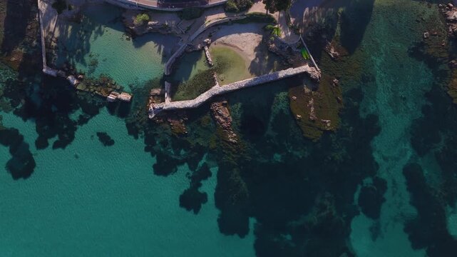 Aerial view of Antibes coastline shows stone breakwater, cove, curved promenade, turquoise waters, submerged rocks, seagrass, golden hour light, and two green kayaks.