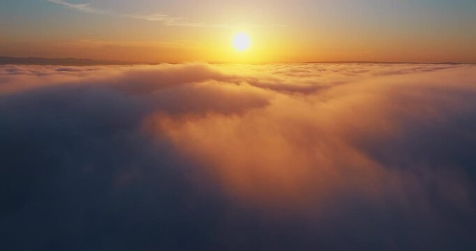 Majestic sunset above clouds aerial shot. Sun light reflecting on cloud surface blue sky background. High altitude drone flight summer travel concept exploration scenic landscape.