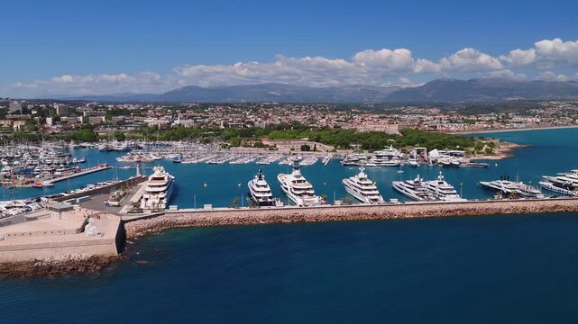 Aerial view of Antibes on the French Riviera shows Port Vauban, Fort Carre, the long stone breakwater, old town blocks, parks, and superyachts under midday light.