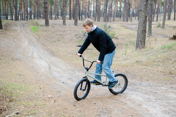 Naklejka premium Teenage Boy Riding BMX Bike on Dirt Path in Pine Forest - Outdoor Extreme Sports and Youth Lifestyle