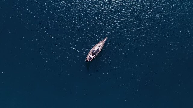 Aerial top down view shows a solitary sailboat drifting off Antibes, France. Sunlight sparkles on ripples, a faint shadow and subtle wake indicate gentle motion.