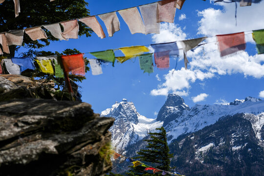 Scenic view from Lama Top in Harshil Valley with colorful Buddhist prayer flags and majestic Himalayan mountains.