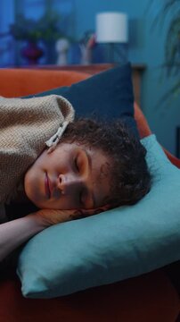 Tired young woman with curly lush hairstyle lying down in bed taking a rest at home room. Carefree girl napping, falling asleep on comfortable sofa with pillows. Closed her eyes enjoy night nap alone