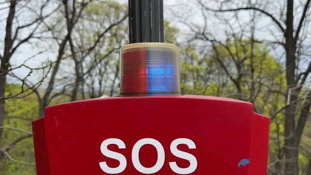 Emergency SOS signal light with blue and red flashing beacon on red pole outdoors in park