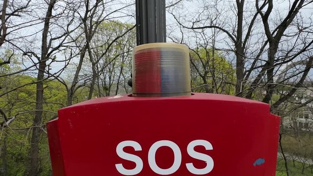 Emergency SOS signal light with blue and red flashing beacon on red pole outdoors in park