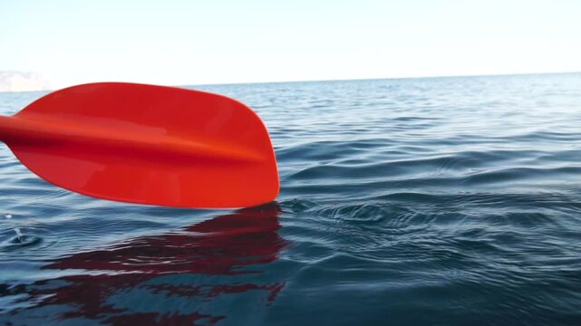 Kayak paddle ocean. Red kayak paddle dipping into calm blue ocean water, creating ripples. Peaceful outdoor activity.