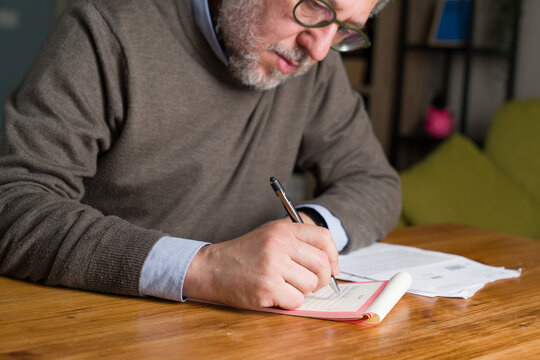 Senior man writing checklist planning tasks at home organizing routine