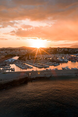 Fototapeta premium Aerial view of Antibes, France at sunset shows the marina with yachts, the compact old town, sandy beaches, and a curved breakwater under soft golden light.