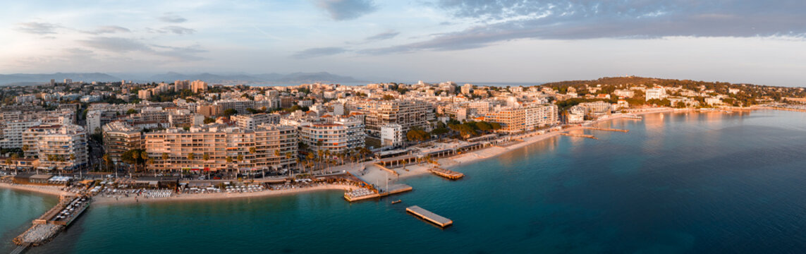 Aerial view of Antibes, France, at sunset shows old town, waterfront, piers, curved promenade, fortified headland, ramparts, and Chateau Grimaldi by a calm bay.
