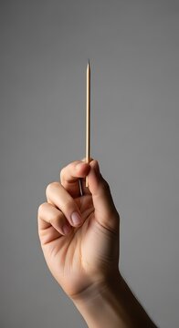 Precise Grip - Hand Holding Slender Metallic Rod Vertically Against Minimalist Grey.