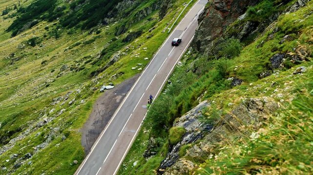 Handheld shot of cyclists riding on the steep Transfagarasan mountain road in Romania. Scenic view of car and bikers on asphalt serpentine winding through rocky alpine landscape