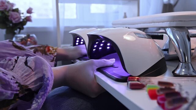 Client cures a fresh gel manicure under twin UV LED nail lamps in a modern salon, capturing violet glow, beauty technology, and the final professional finishing stage.
