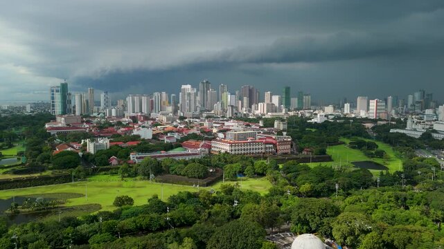 Drone rises above Baluarte de San Diego ruins in Intramuros revealing historic colonial district and modern Manila skyline under dramatic dark storm clouds