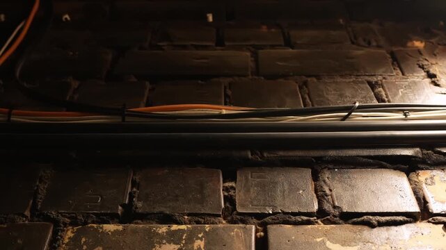 Warm close-up of backstage electric cables and conduits running across a brick wall, revealing hidden theater infrastructure, technical wiring, and industrial texture.
